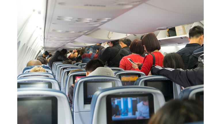 People are standing and sitting in an airplane cabin before disembarking.
