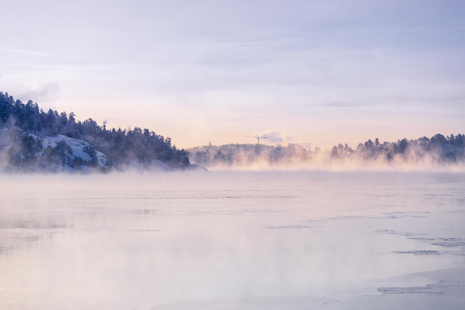 Frozen lake with fog under sky at sunrise
