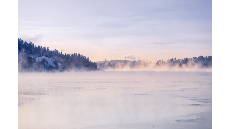 Frozen lake with fog under sky at sunrise