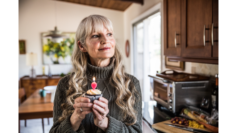 Woman (60yrs) holding cupcake with birthday candle