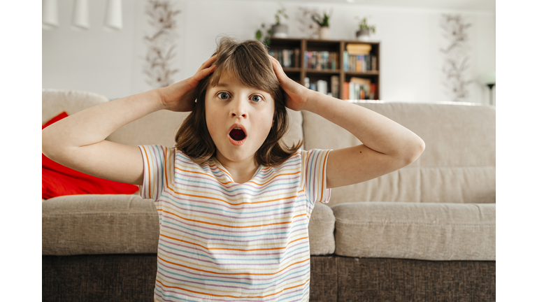 Surprised girl with head in hands near sofa at home