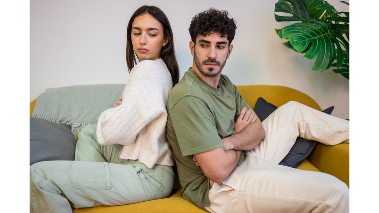 Young couple sitting on a sofa with their backs to each other.