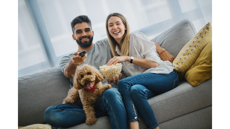 Young couple laughing while watching their favorite series on TV.
