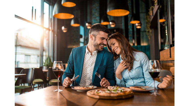 Playful couple eating pizza together in a restaurant.