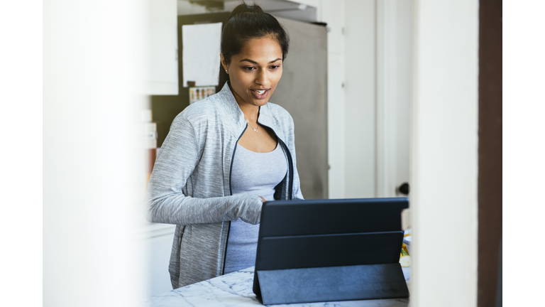 Woman video chatting on digital tablet in kitchen at home