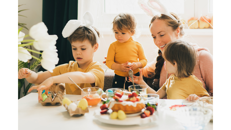 Family with three children painting Easter eggs at cozy home.