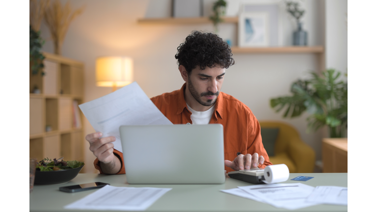 Front view of a young man checking bills in his apartment.