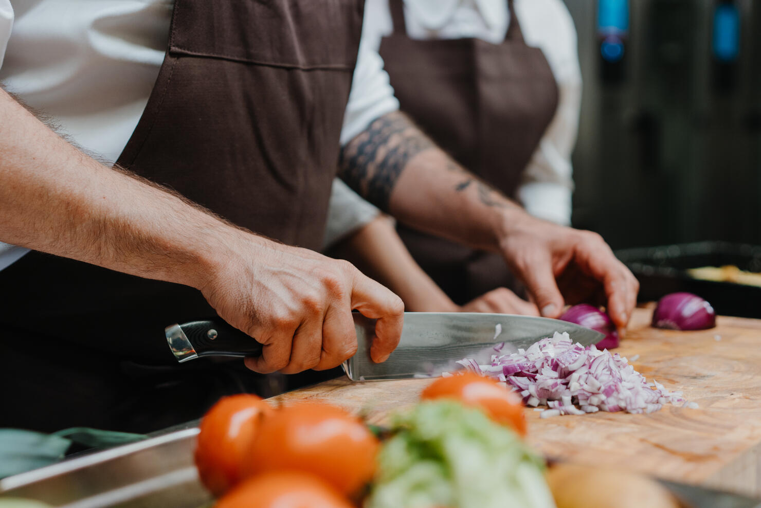 Close-up of chef cutting onion on cutting board in restaurant kitchen.
