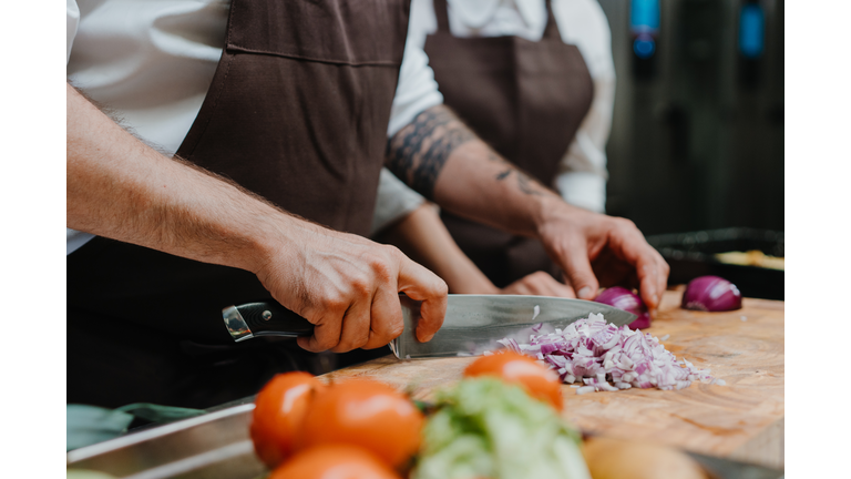 Close-up of chef cutting onion on cutting board in restaurant kitchen.