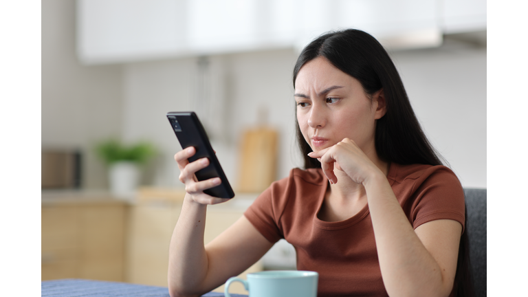 Suspicious asian woman checking phone in the kitchen