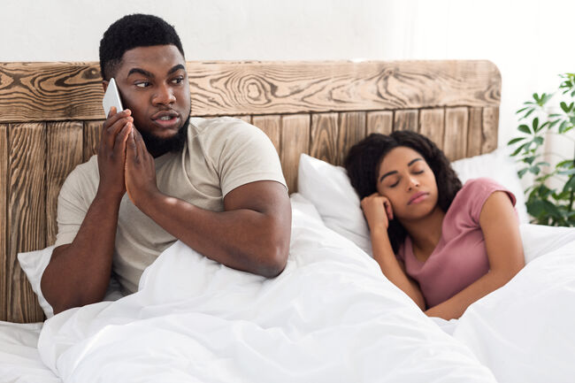 Black guy talking with lover on cellphone in bed