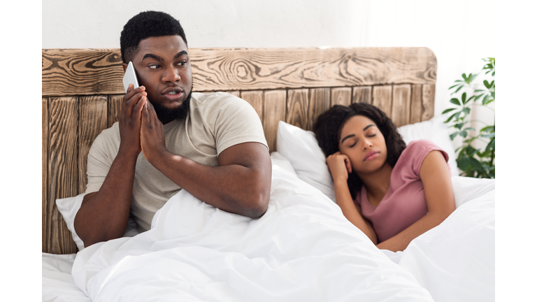 Black guy talking with lover on cellphone in bed