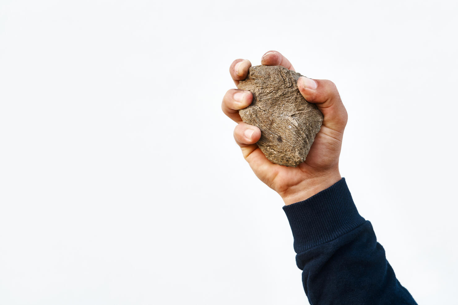 Man's hand holding a stone to be thrown at a victim of the execution sentence by stoning.