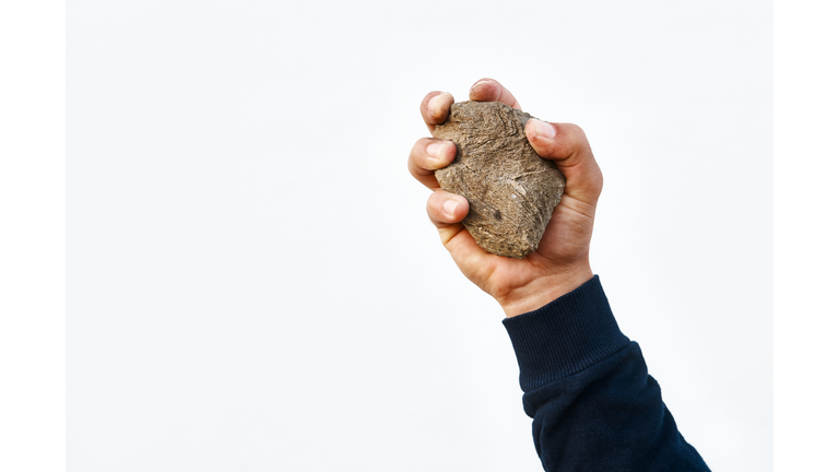Man's hand holding a stone to be thrown at a victim of the execution sentence by stoning.