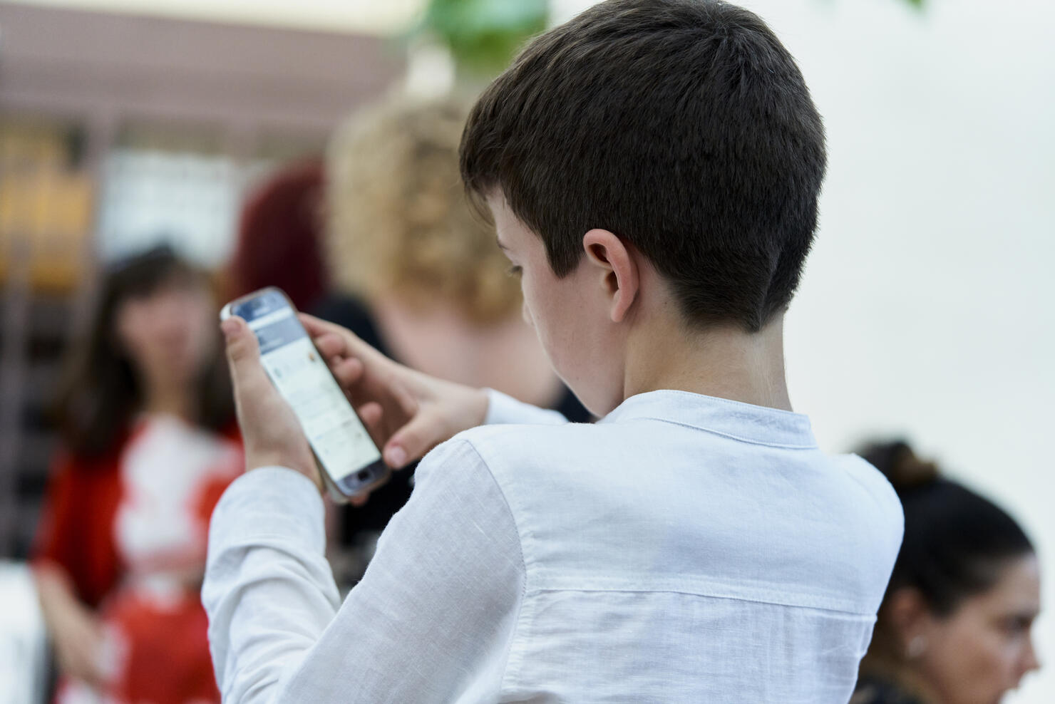 boy sitting in soft shirt in a group of people concentrating on using a telephone