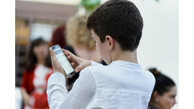 boy sitting in soft shirt in a group of people concentrating on using a telephone