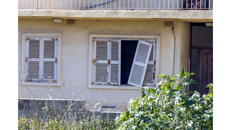 Detail of abandoned grunge yellow stone rural house with broken window and cactus growing in the garden