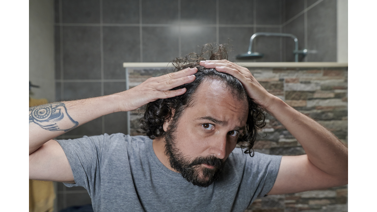 Man looking at his hair in bathroom mirror