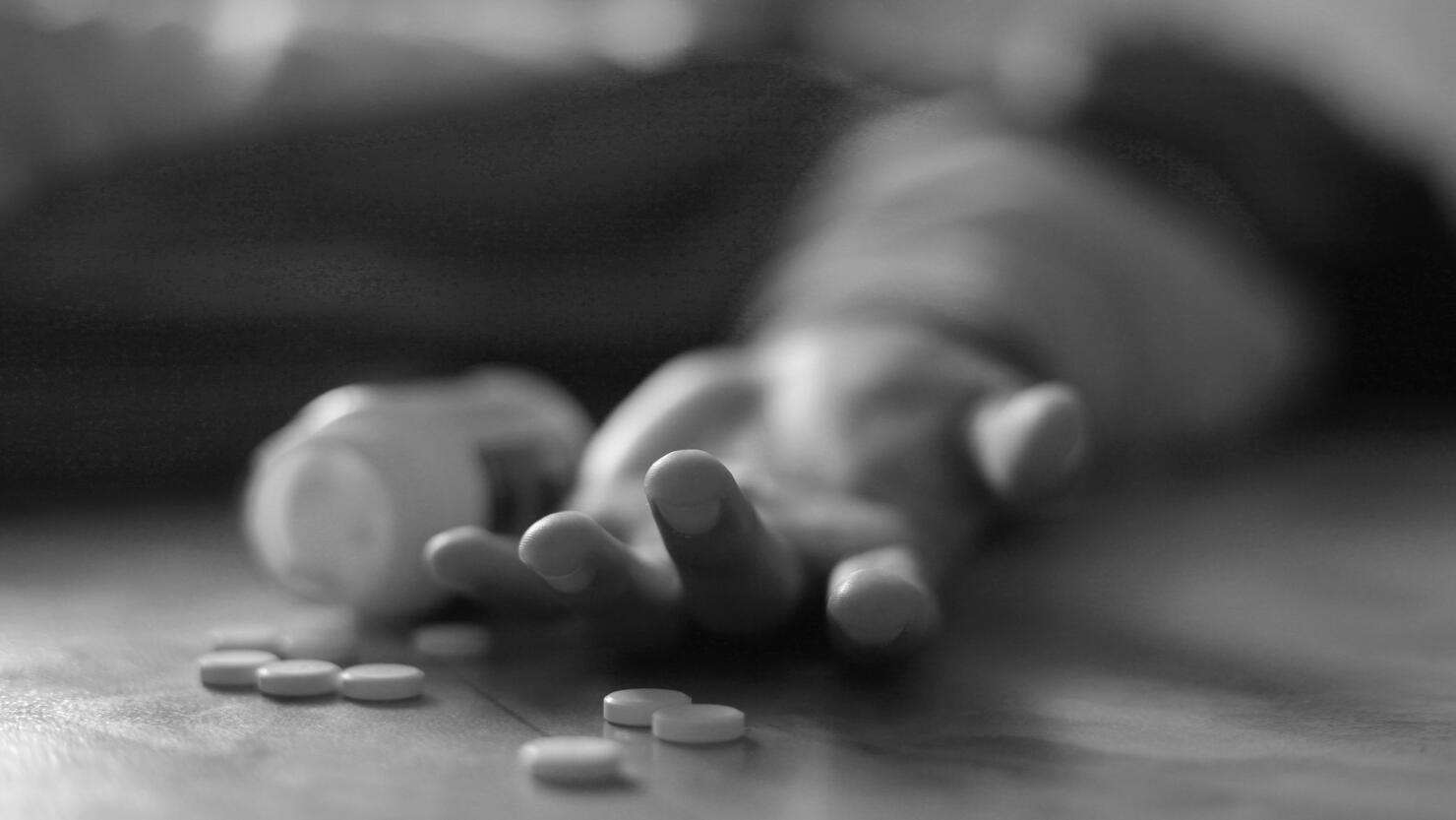 Man lying on the floor, unconscious or dead due to drugs abuse, focus on fingers with pills