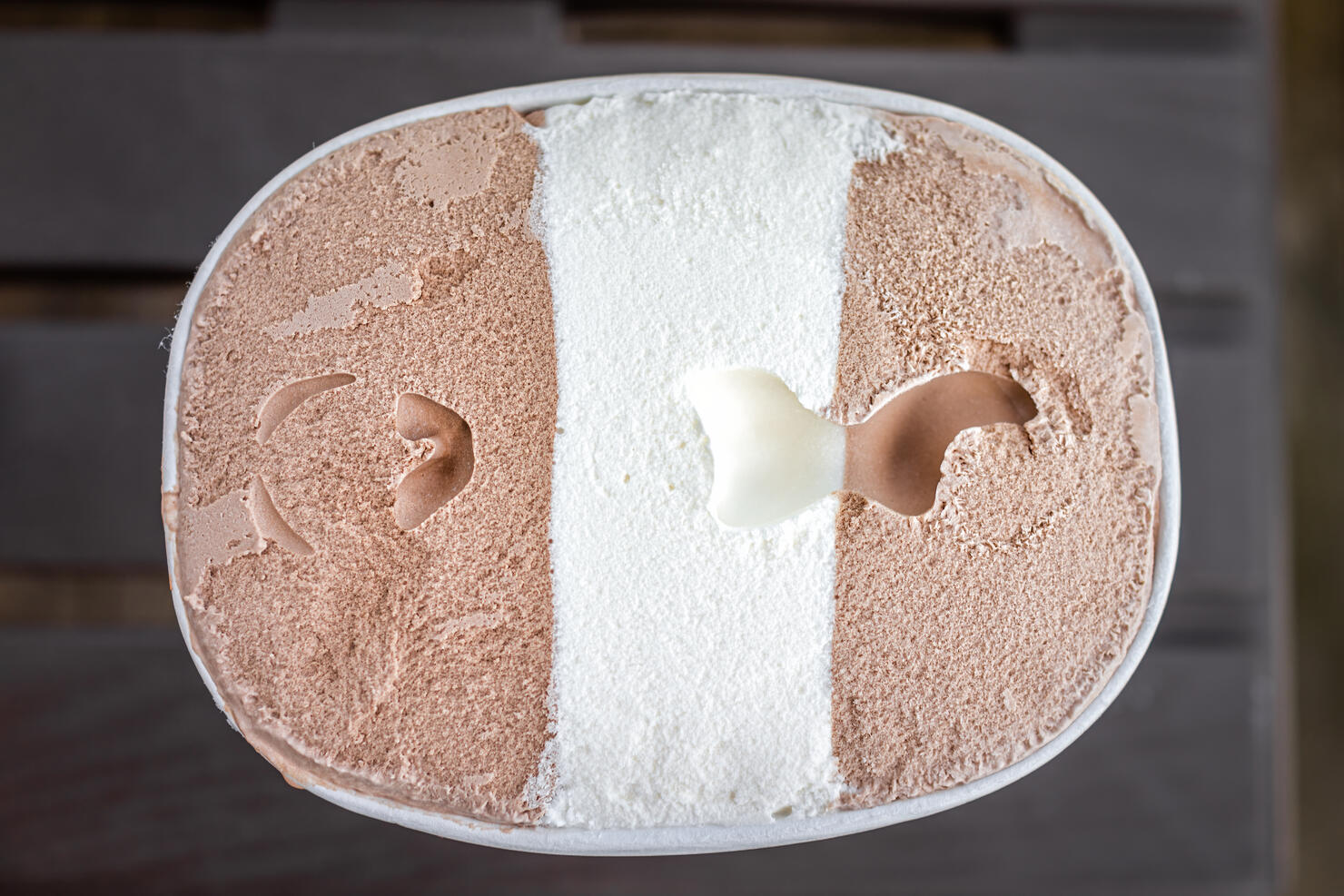 Flat top lay view of container carton of dark and milk chocolate vanilla neapolitan ice cream frozen dessert gelato storebought with texture of dairy cream three flavors