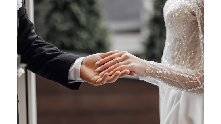 The man gently holds the bride's hand with a beautiful golden wedding ring. Enlarged image of newlyweds' hands. Wedding concept. The groom gently touches the bride