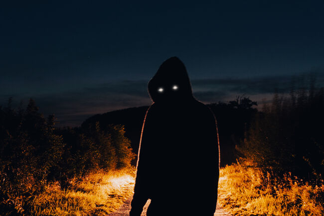 A horror concept of a scary hooded figure with glowing eyes. At night back lighted in the countryside