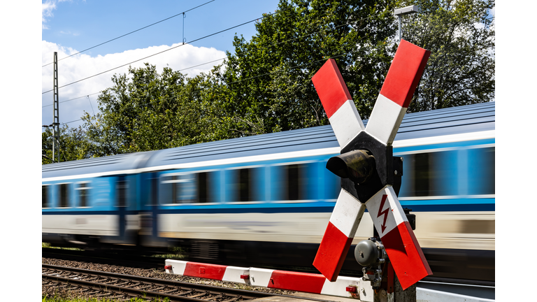 Closed barrier at a railroad crossing with fast passing passenger train