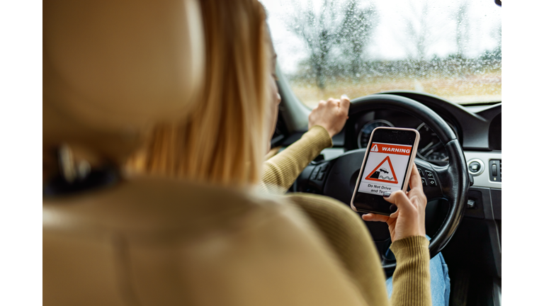 Woman Using Mobile Phone While Driving a Car with sign on her smartphone.