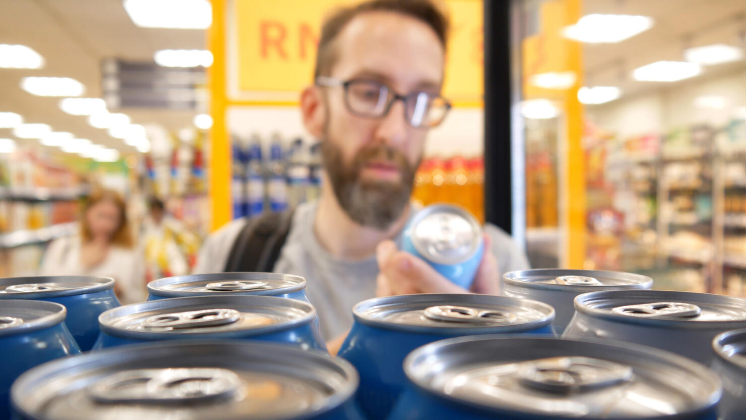Close-up of many aluminum cans of beer in a store fridge and a male buyer choosing one