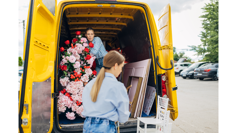 Two event planners bring chairs, flower arrangements and other party decorations out of the trunk of a van