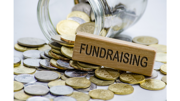 Fundraising text on wooden block with coins and jar background. Charity concept