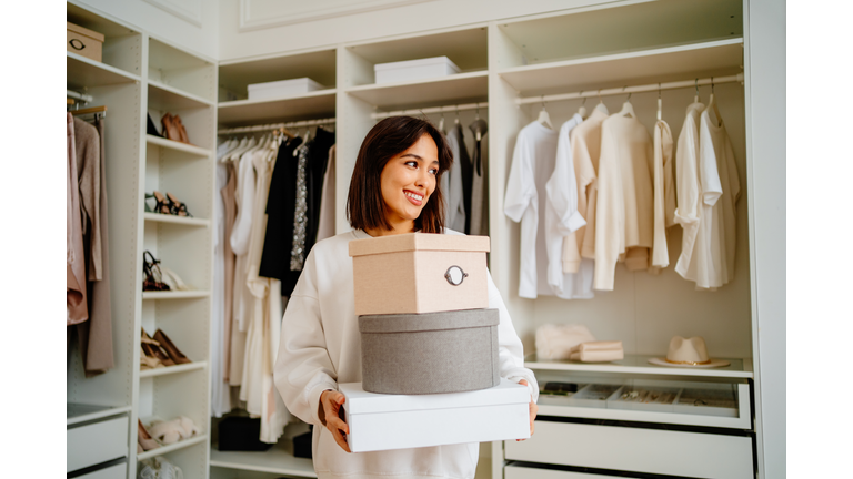 Get rid of excess clothes. Smiling woman carrying clothes boxes in hands near walk in wardrobe