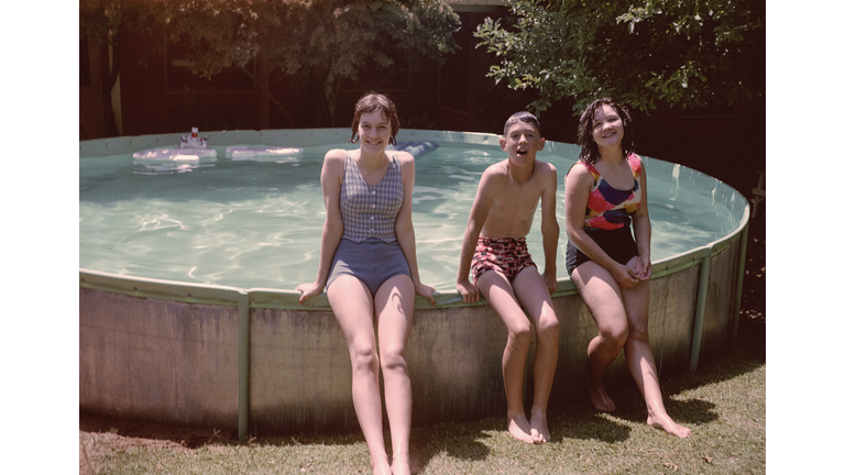 Portrait of Caucasian brother and sisters leaning on swimming pool