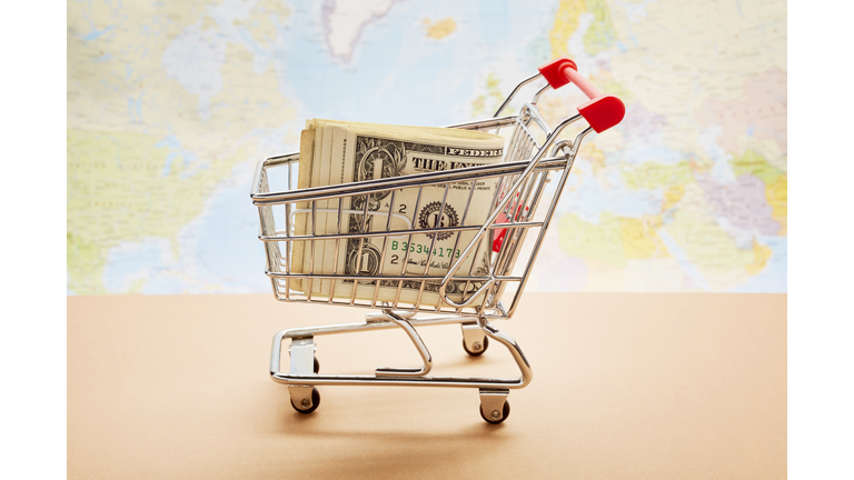 Still life of a small shopping cart with American Dollar banknotes against world map