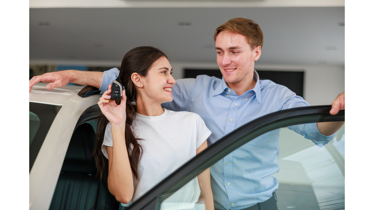 Happy couple excitedly holding car key of their new purchase inside a modern car dealership showroom; capturing the joyful moment of buying a new vehicle with customer satisfaction