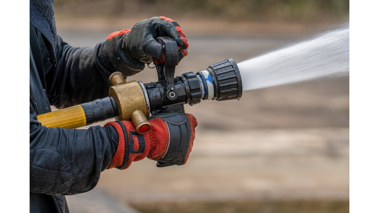 Close up hands of firefighter spraying high pressure water to fire.