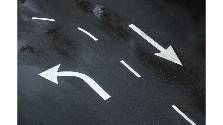Two directional signs with white turn left arrow and right go straight arrow painted on asphalt