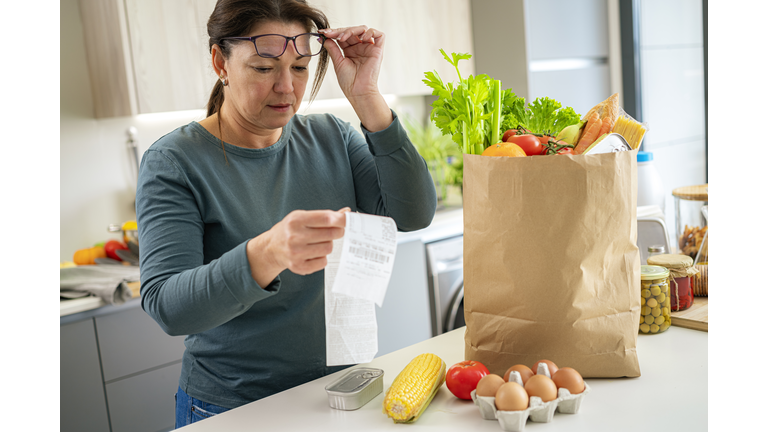 Surprised woman checking supermarket receipt after buying groceries