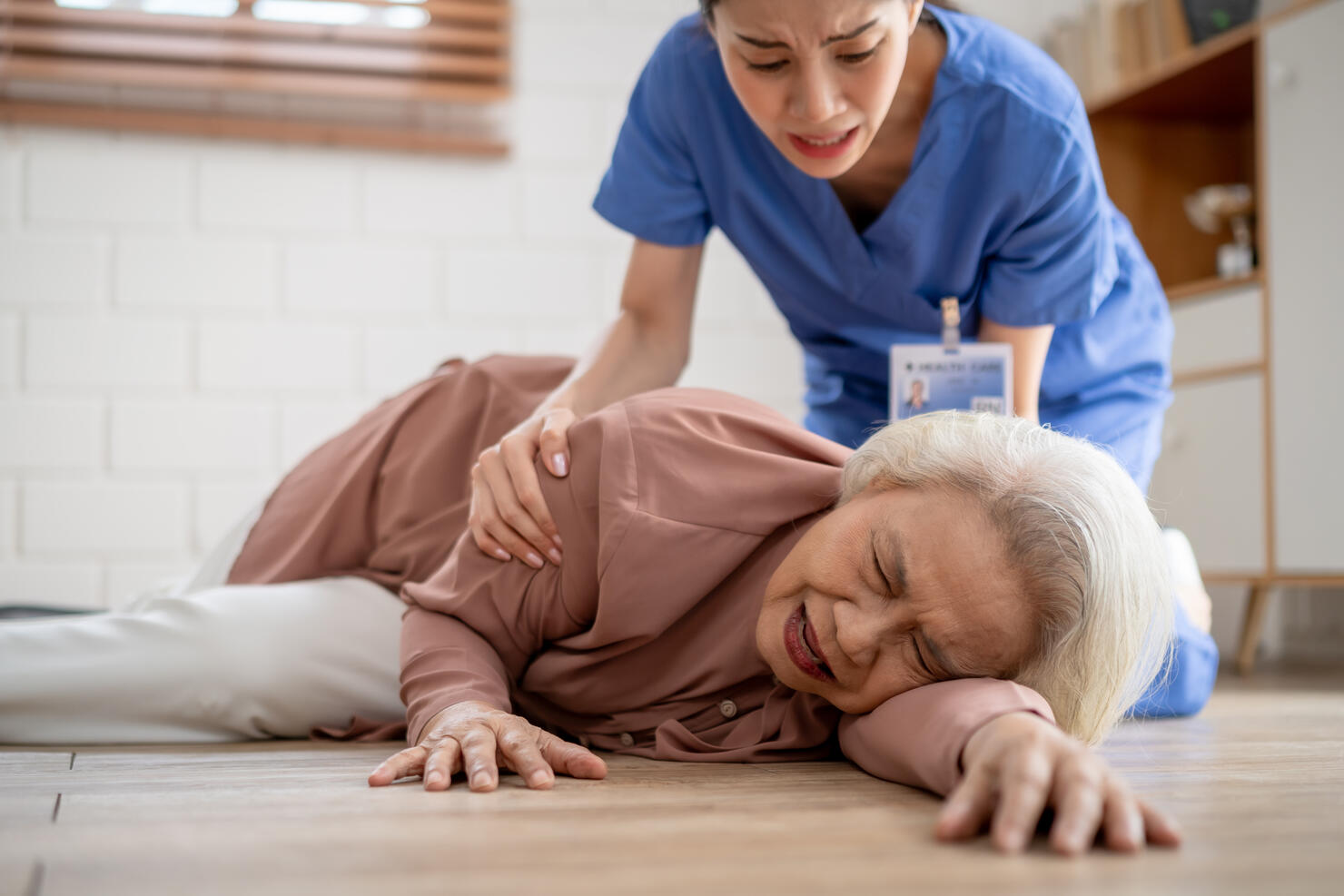 Asian caregiver help senior female from falling on the ground at home. Elderly older patient having an accident while doing physical therapy then rescued by attractive therapist nurse in living room.