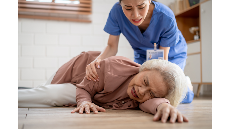 Asian caregiver help senior female from falling on the ground at home. Elderly older patient having an accident while doing physical therapy then rescued by attractive therapist nurse in living room.
