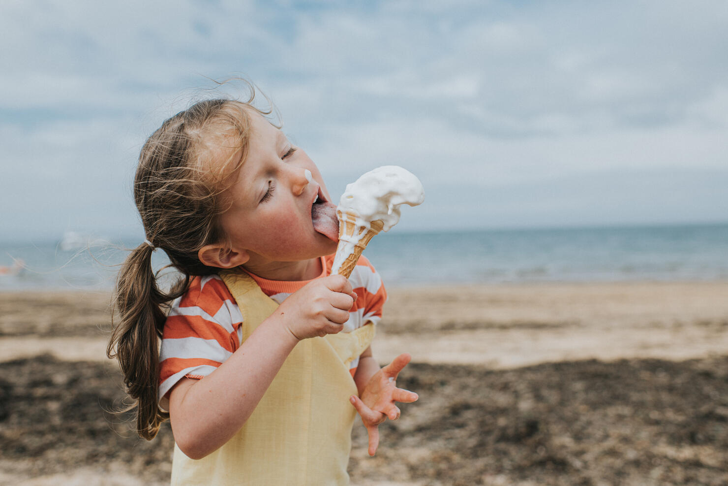 A little girl stands on a beach and eats a melting ice-cream
