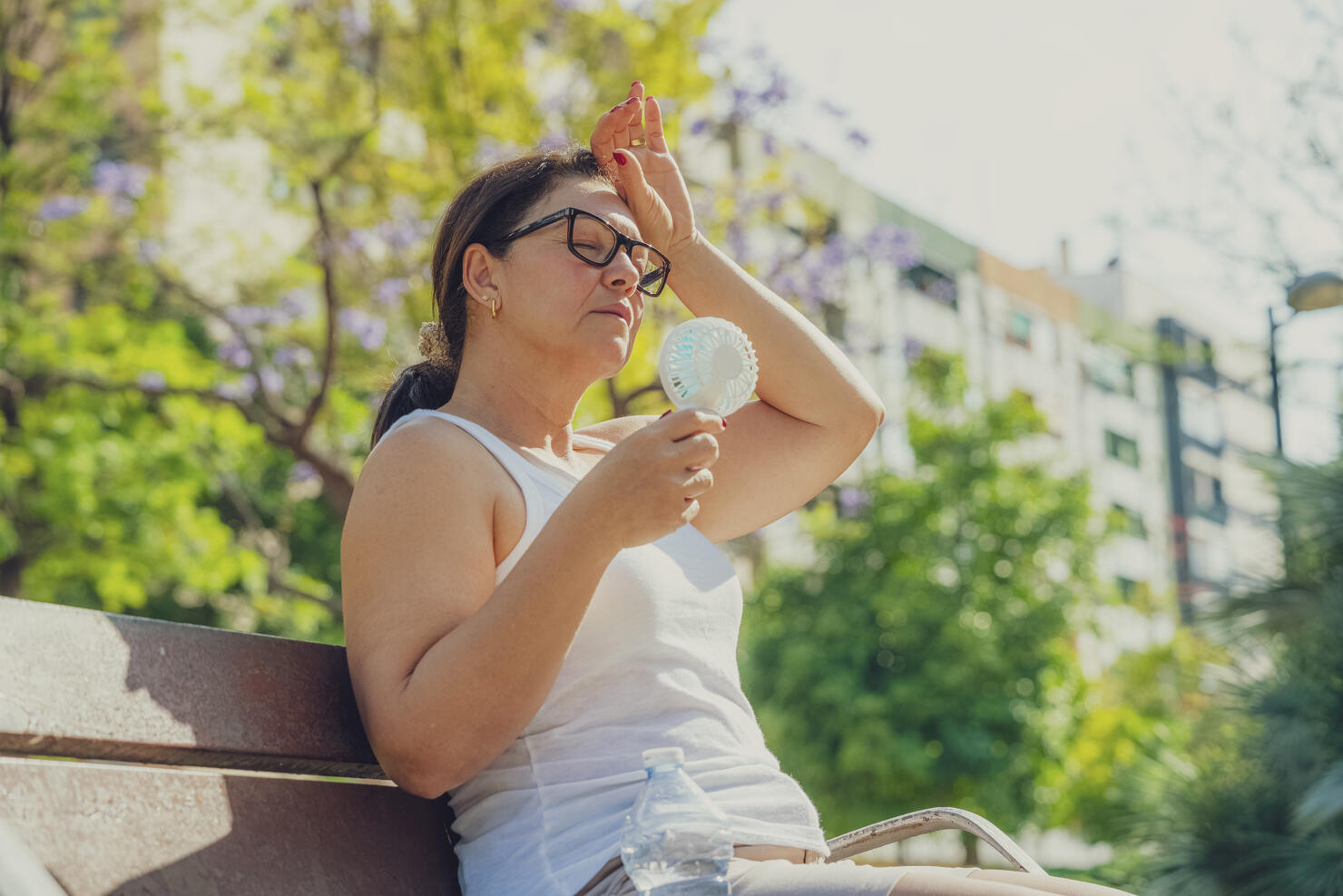 Woman suffering from heat stroke and headache. Holding an electric mini fan sitting outdoors