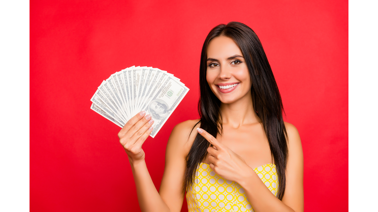 Close up portrait of excited beautiful gorgeous attractive pretty cheerful confident dark-haired woman demonstrating fan made of money and pointing with forefinger isolated on vivid red background