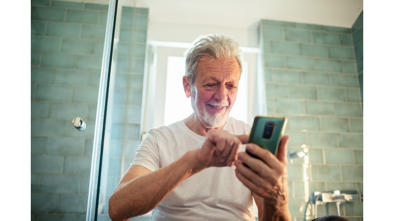 Senior man using a smart phone in a bathroom