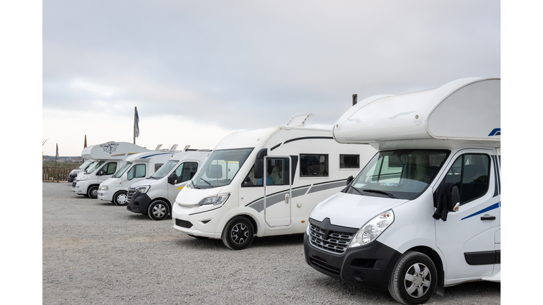 Group of white motorhomes parked in the parking lot of a campsite.