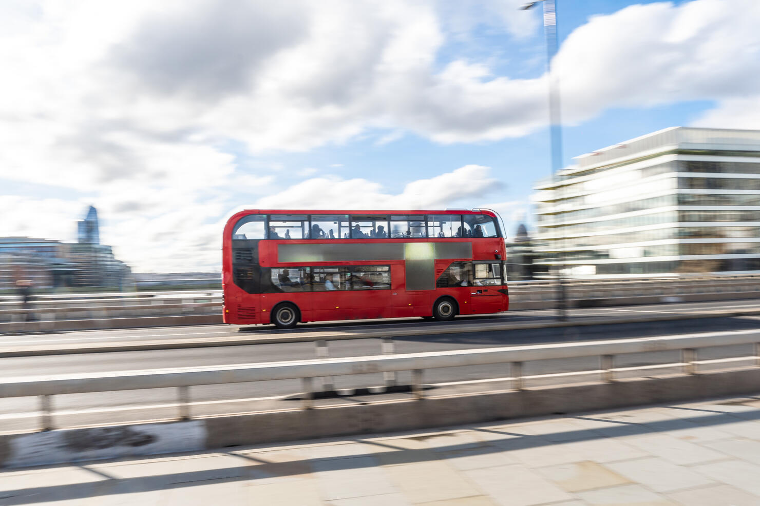 Red double-decker bus crossing london bridge on a sunny day