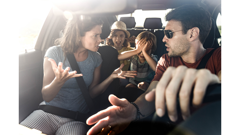 Frustrated parents arguing during trip by a car.