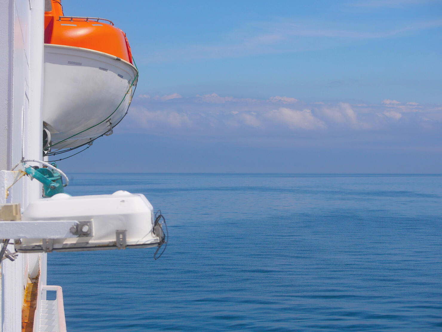 Lifeboat on the deck of a ferry cruise ship. Saving lives on the water concept. Side view against the background of the sky and calm sea in sunny weather.