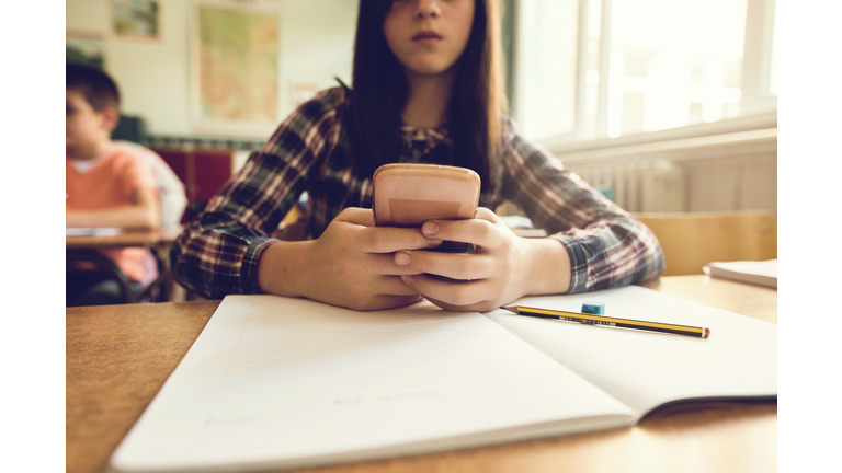 Close up of schoolgirl using mobile phone in the classroom.