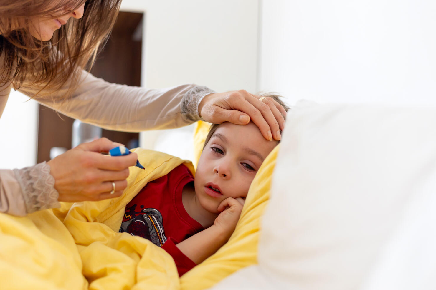 Sick child, toddler boy lying in bed with a fever, having breakfast, resting at home